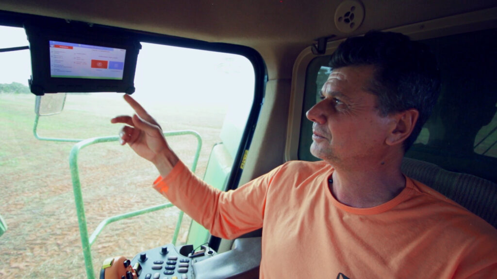 Operador com bordo Solinftec, ilustrando monitoramento agrícola em tempo real com interação com equipes no campo.